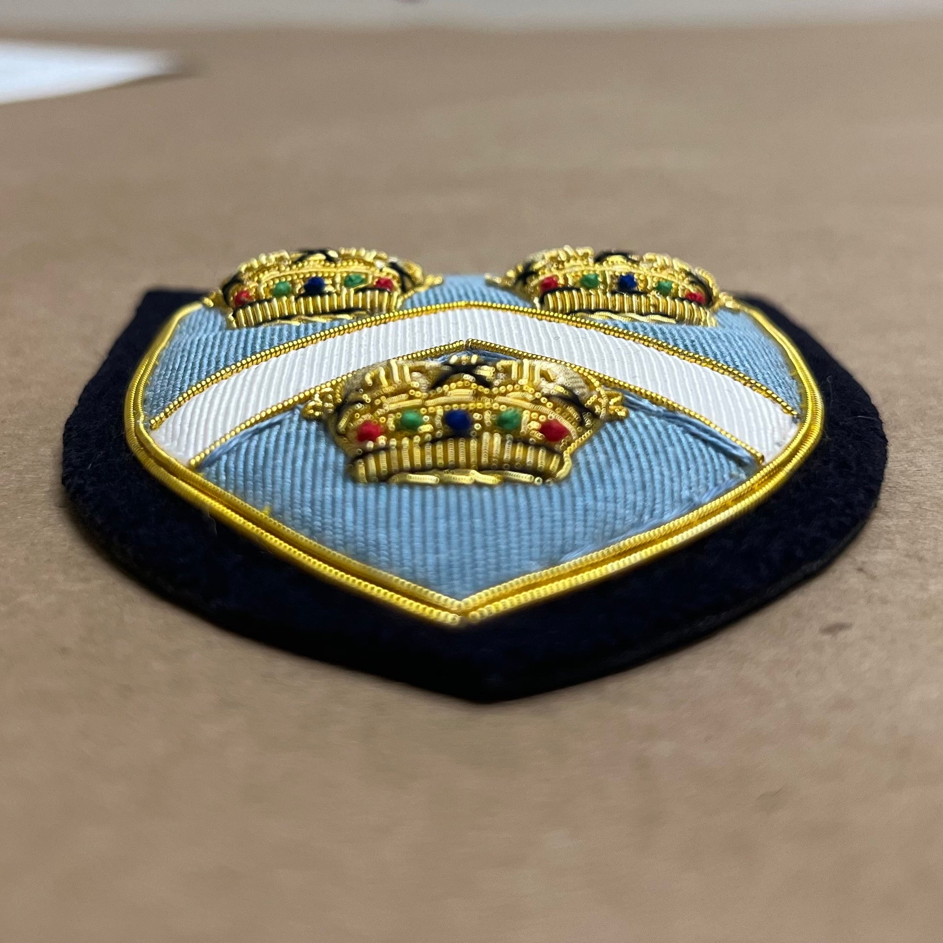 3D Embroidered patch with a blue shield design and gold crowns on a beige background